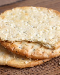 Three golden cheese crackers on dark wood board.