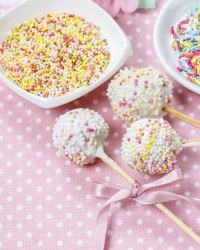 White cake pops on pink dotted table cloth. Colorful sprinkles